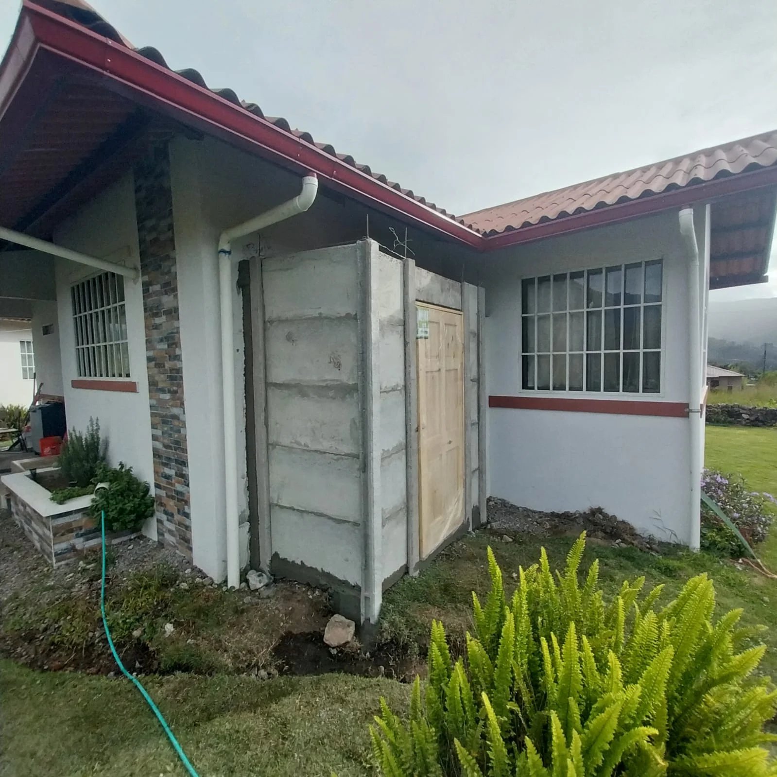 Anexo de muros de concreto recién instalado entre dos viviendas en jardín residencial